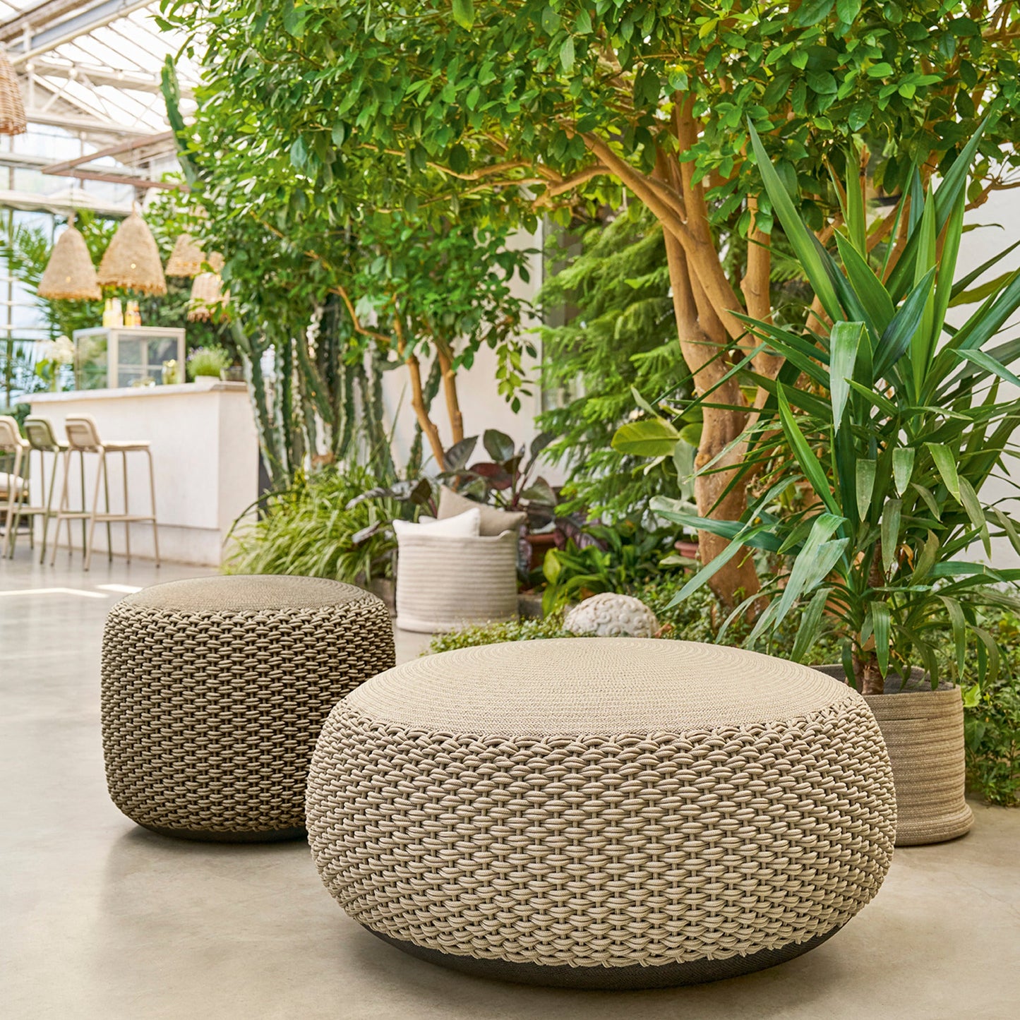 Weishäupl Pouf groß Sand und medium Taupe zwischen Pflanzen auf der Terrasse