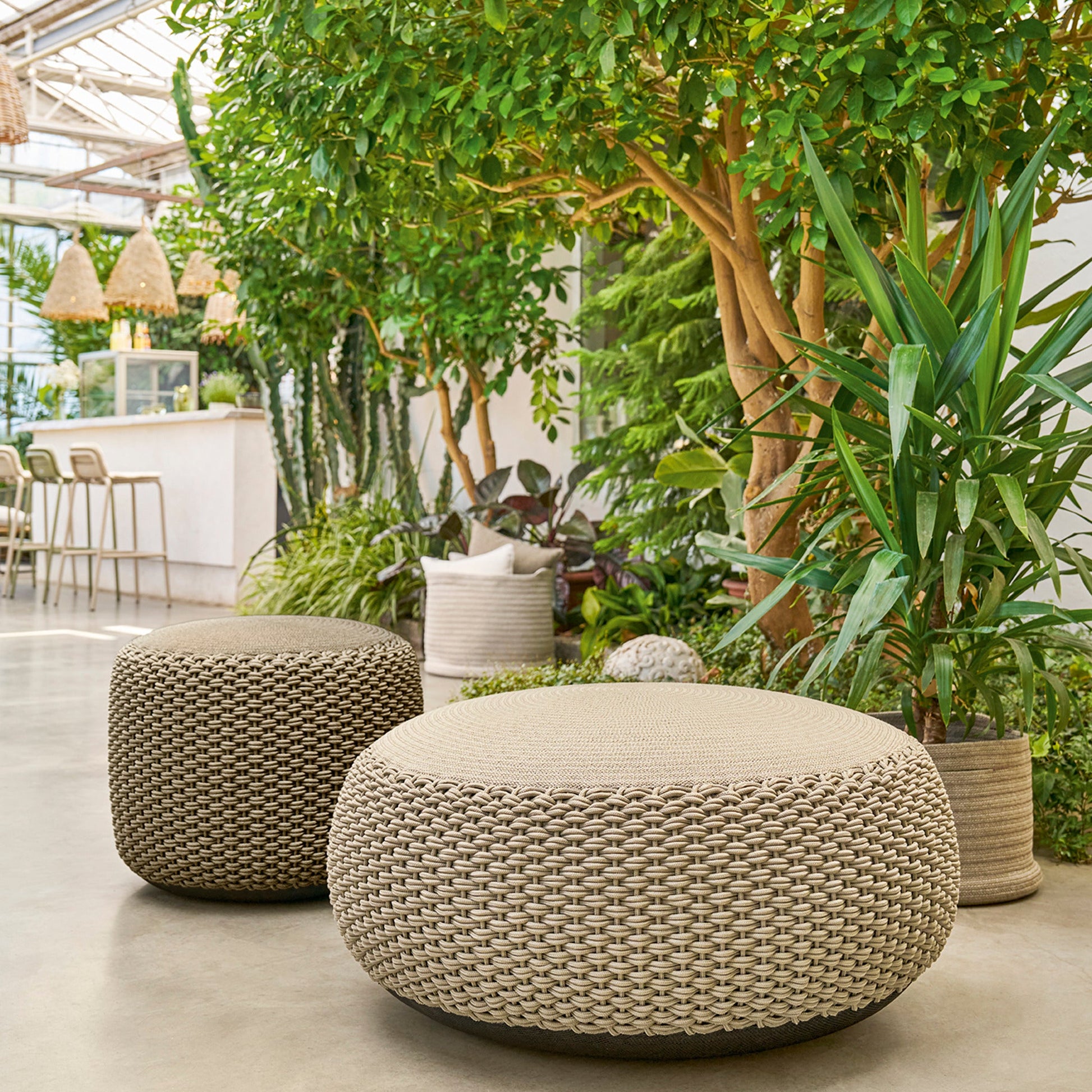 Weishäupl Pouf groß Sand und medium Taupe zwischen Pflanzen auf der Terrasse