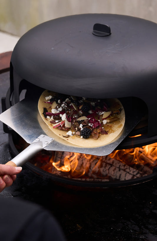 OFYR Pizza Oven 100 auf der OFYR Feuerplatte in mediterranem Garten