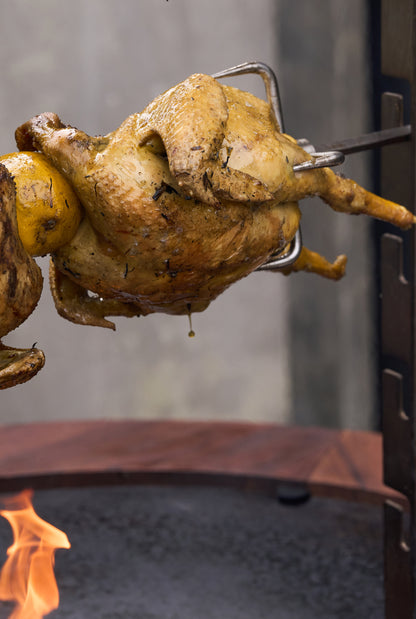 Hähnchen dreht sich am Spieß des OFYR Rotisserie Set über dem Feuer