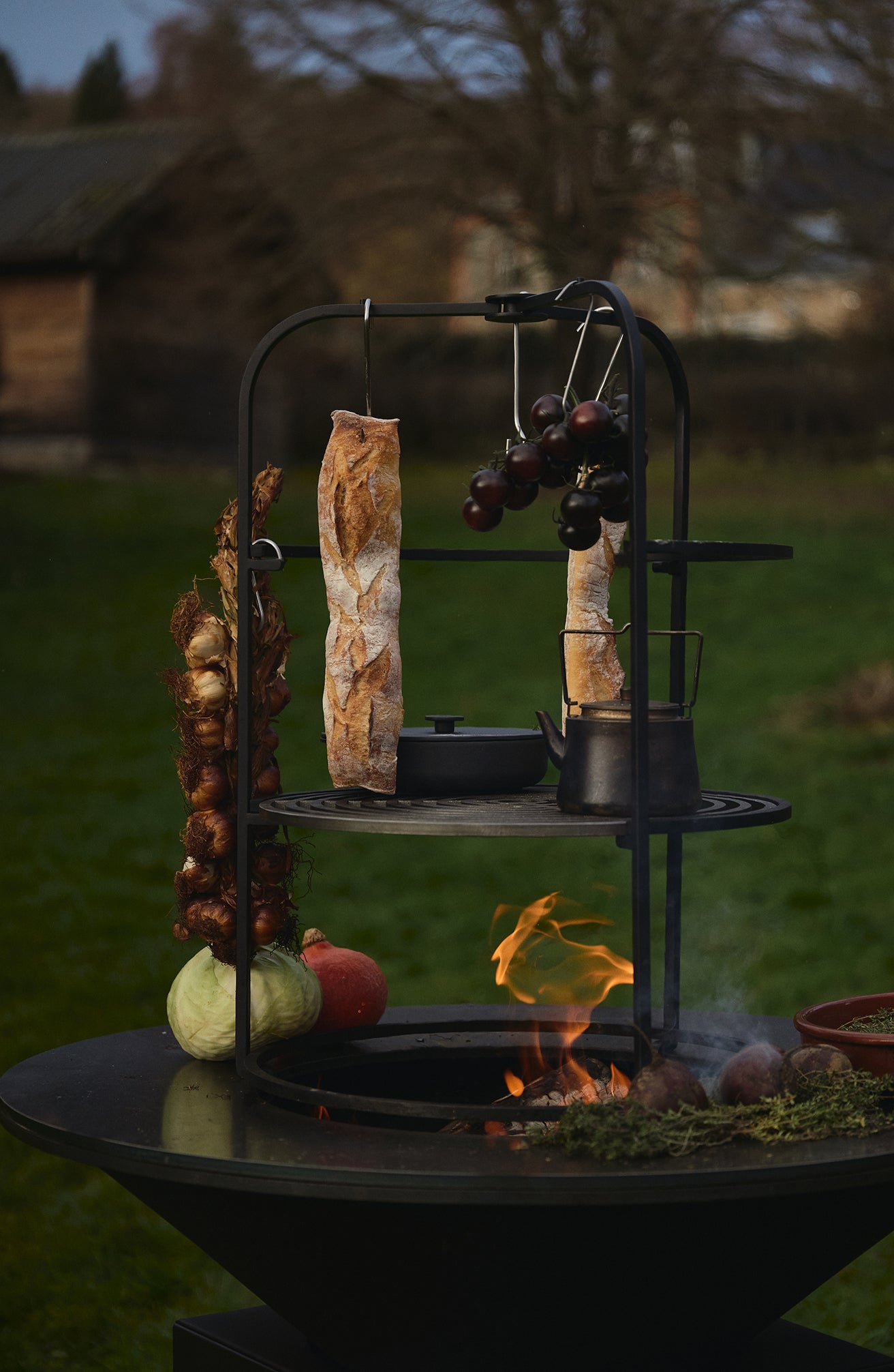 OFYR Cage 100 mit aufgehängtem Brot, Zwiebeln und Kessel auf dem Grillrost über dem Feuer