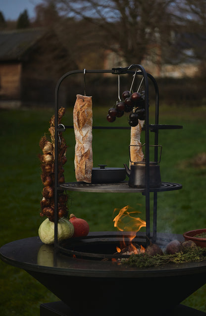 OFYR Cage 100 mit aufgehängtem Brot, Zwiebeln und Kessel auf dem Grillrost über dem Feuer